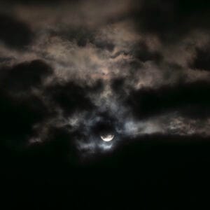 A dark night with a bright moon highlighting the passing clouds.